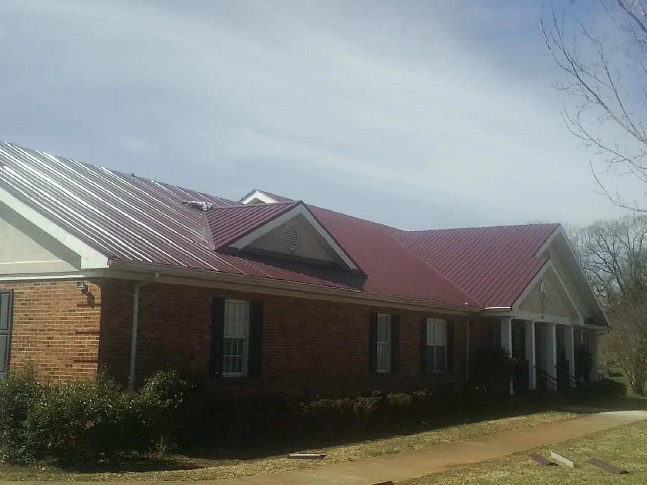 Red metal roof with gabled entries on a long brick building, from a Hail Damage Roof Repair job in Flanders