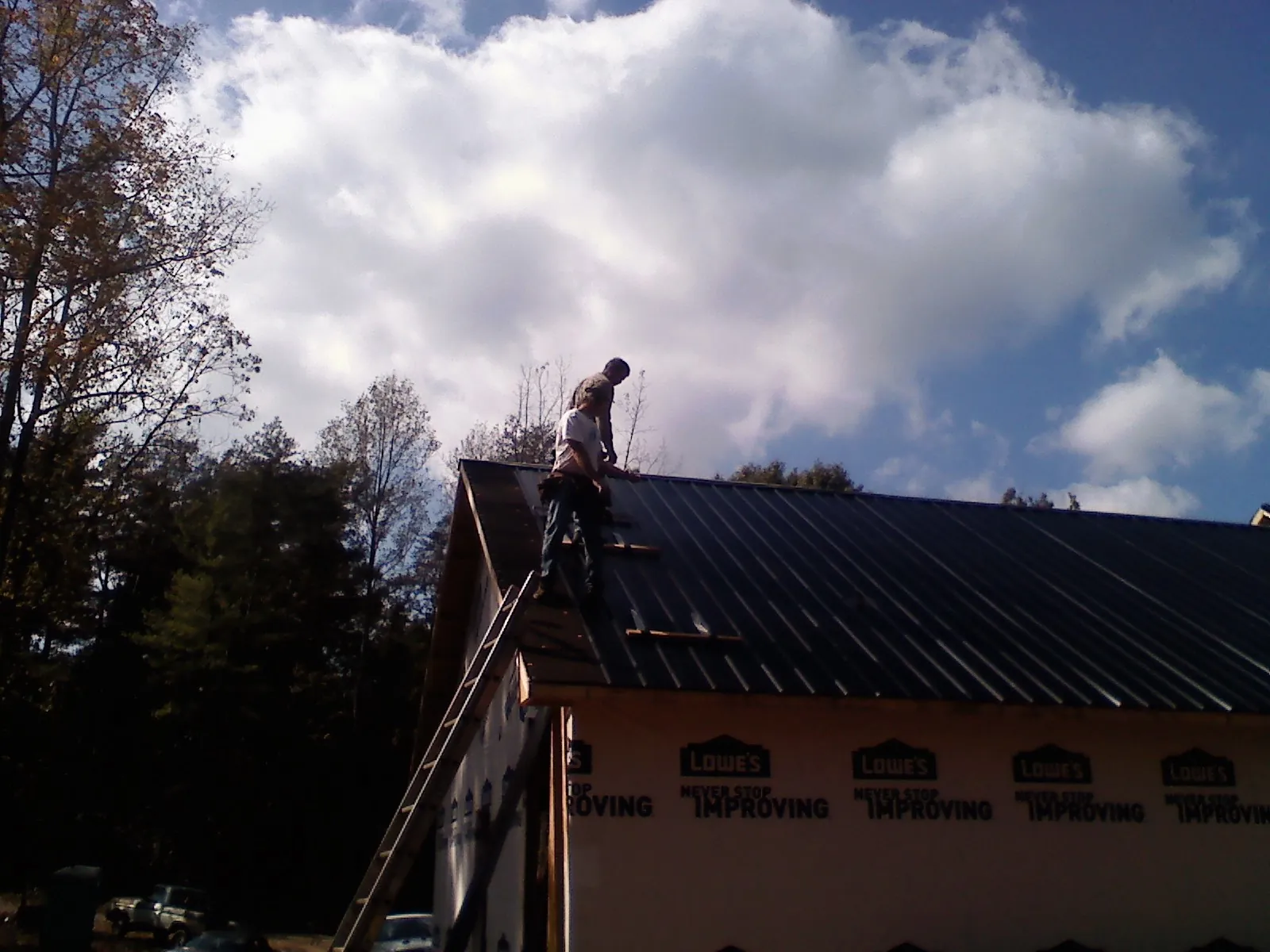 Roofer fastening dark metal panels high against a cloudy sky, from a Roof Inspection job in Flanders